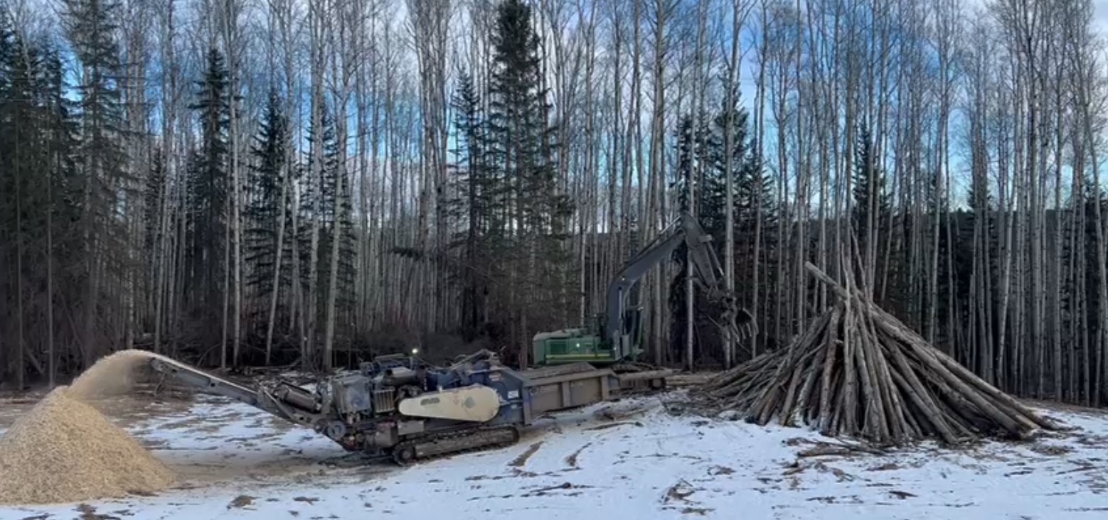 A horizontal grinder and loader working together to turn an unburned pile of waste wood into reusable wood fibre